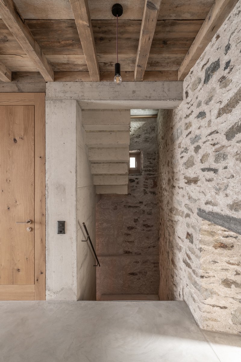 Entry hall with timber ceiling, stone walls, and concrete stair tower lit by pendant fixture