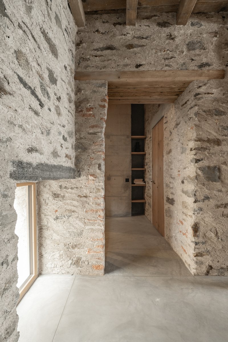 Corridor view between exposed stone walls with timber beams above and polished concrete floor