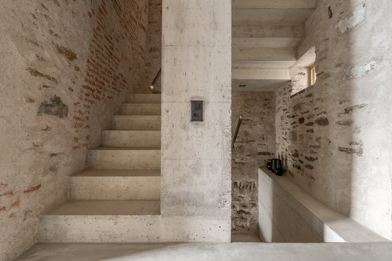 Concrete staircase ascending alongside a structural column within stone and brick walls