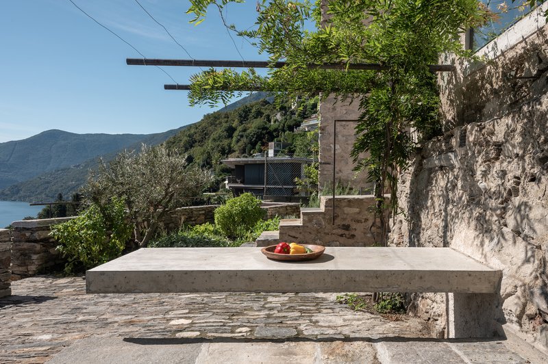 Concrete table on stone terrace overlooking water and wooded hillside under summer sky