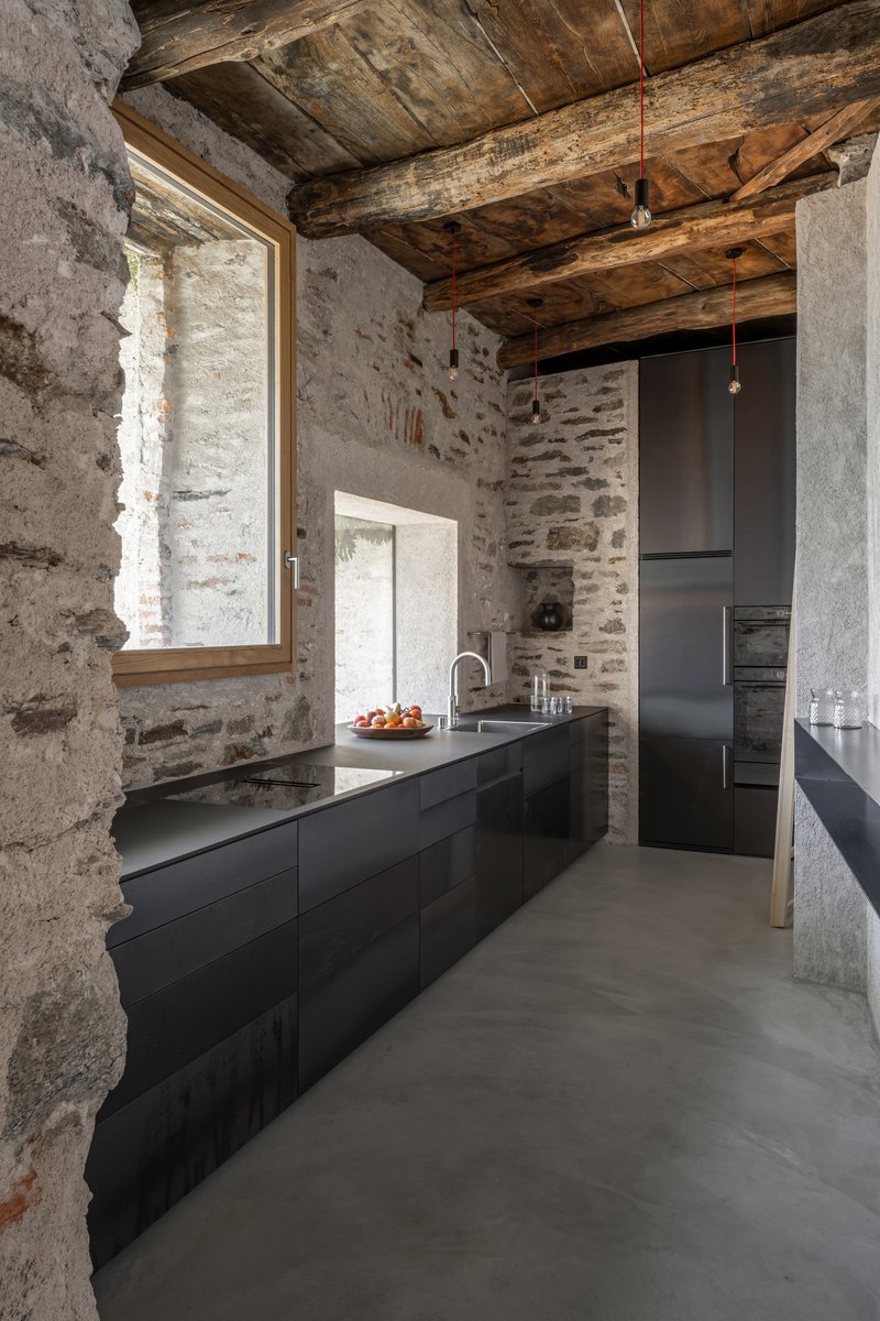 Kitchen with black cabinetry beneath timber ceiling and stone walls with casement window