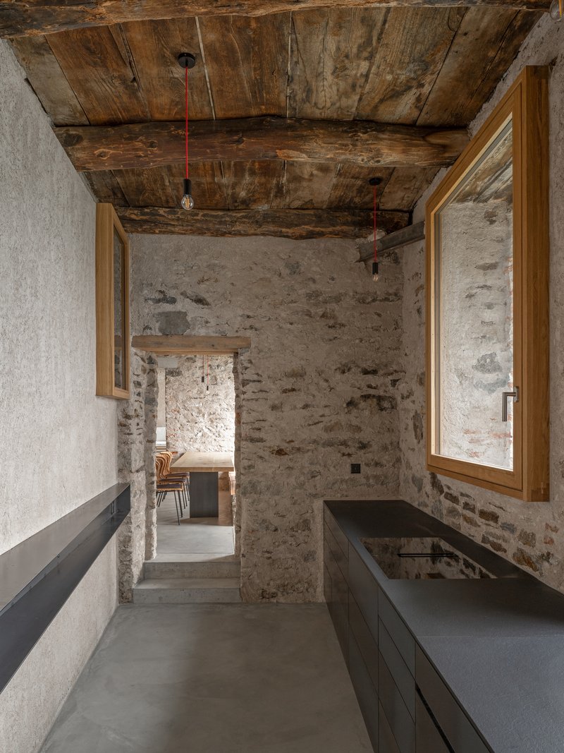 Interior passage with dark cabinetry along rough stone walls under timber plank ceiling with pendant lights