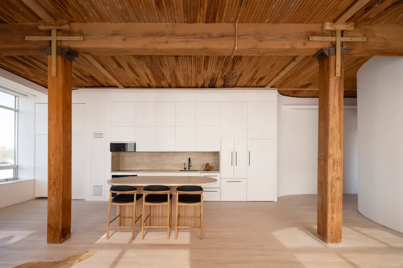 Kitchen area framed by exposed timber beams and columns with slatted wood ceiling in afternoon light