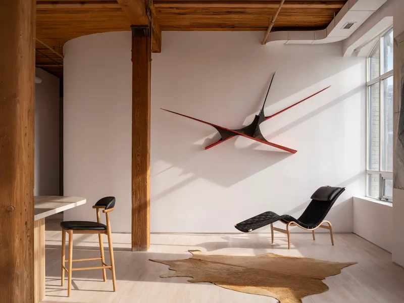 White wall with sculptural black and red artwork above a chaise lounge near sunlit windows