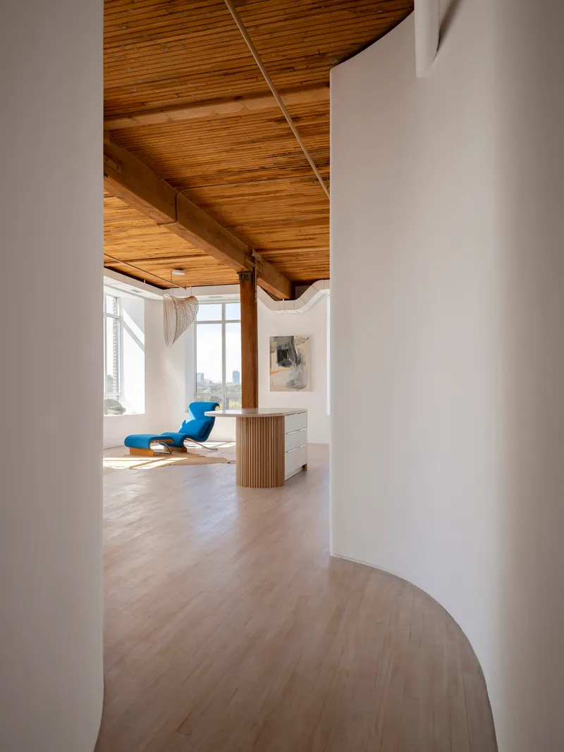 View through curved white walls into a workspace with timber desk and blue chair