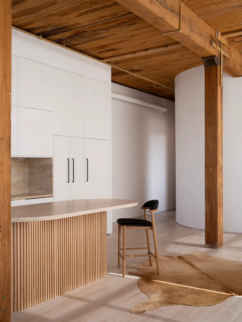 Counter with vertical timber slats beneath white cabinetry and exposed structural beams