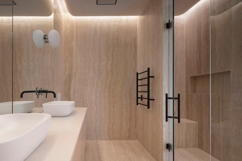 Bathroom with travertine walls, cove lighting, glass shower enclosure and floating double vanity