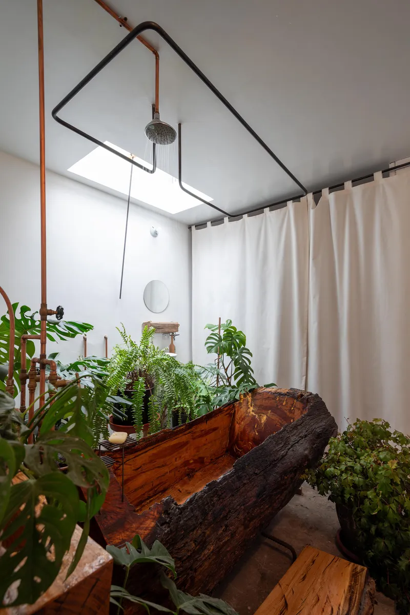 Bathroom with curved timber bathtub carved from a log surrounded by potted plants