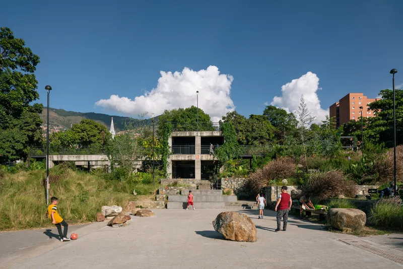 Concrete plaza with large boulders and visitors beneath puffy white clouds and distant mountains