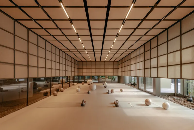 Long exercise hall with continuous gridded screen walls and scattered ceramic vessels on polished floor