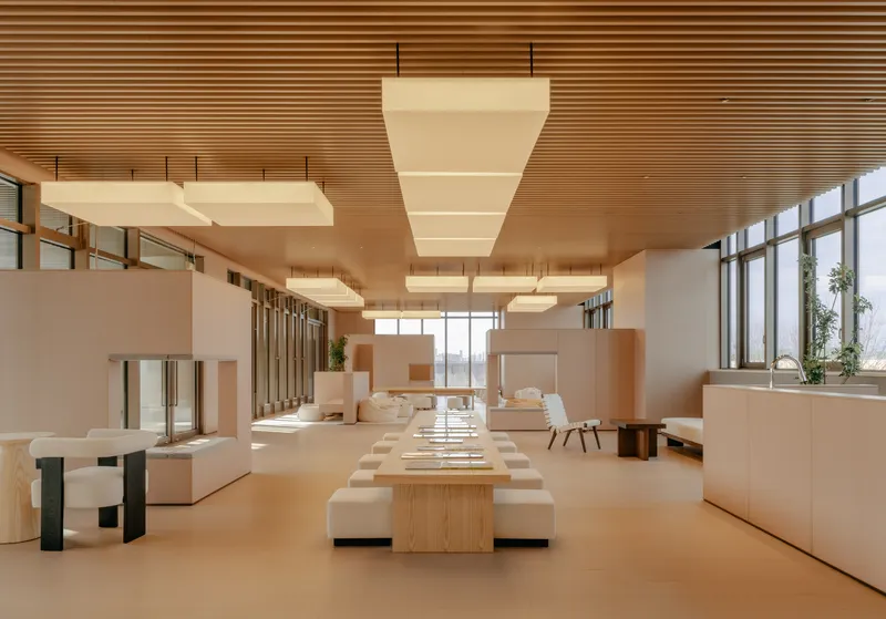 Open office interior with horizontal timber slat ceiling and suspended cubic light fixtures above communal tables