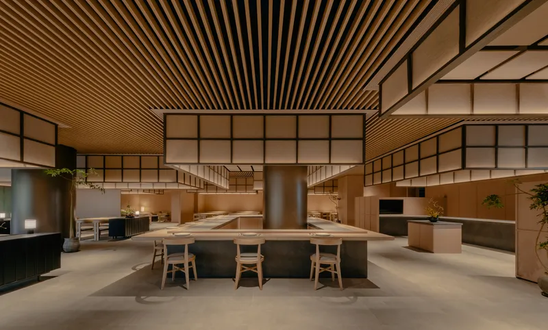 Double-height dining space with translucent gridded screens and a central cylindrical metal column in evening light