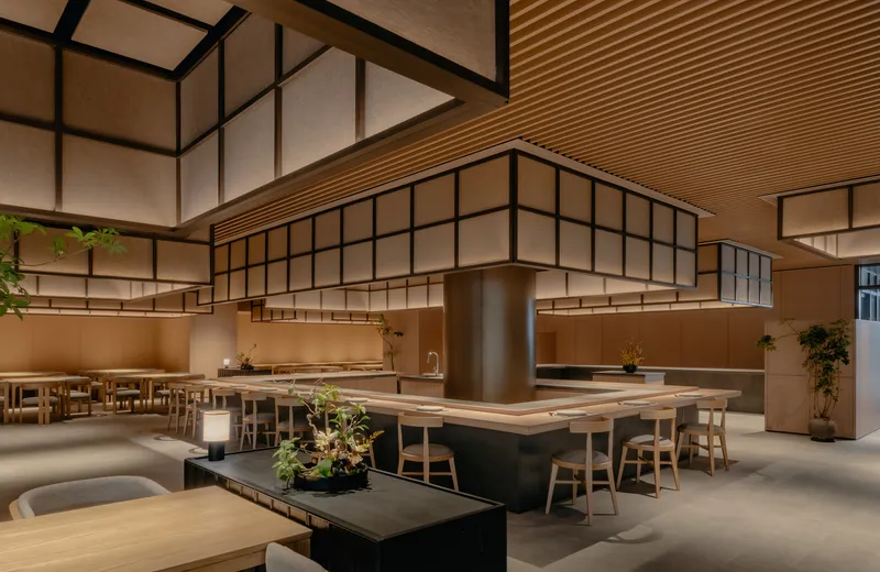Restaurant interior featuring communal timber tables with planted center dividers and floating gridded partition walls