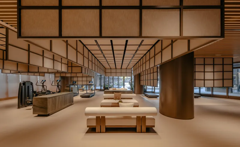 Fitness room with slatted wood ceiling, translucent panel walls, and upholstered benches in warm ambient light