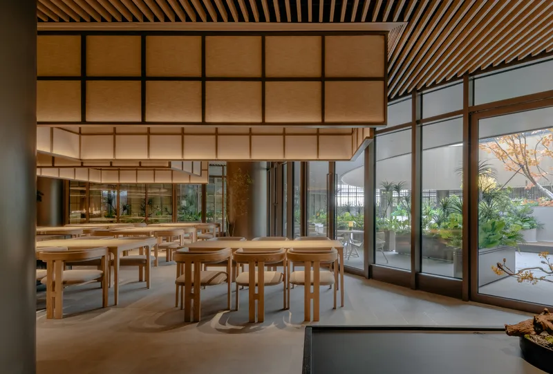 Dining area with timber tables and stools beneath a gridded wood ceiling and translucent panels