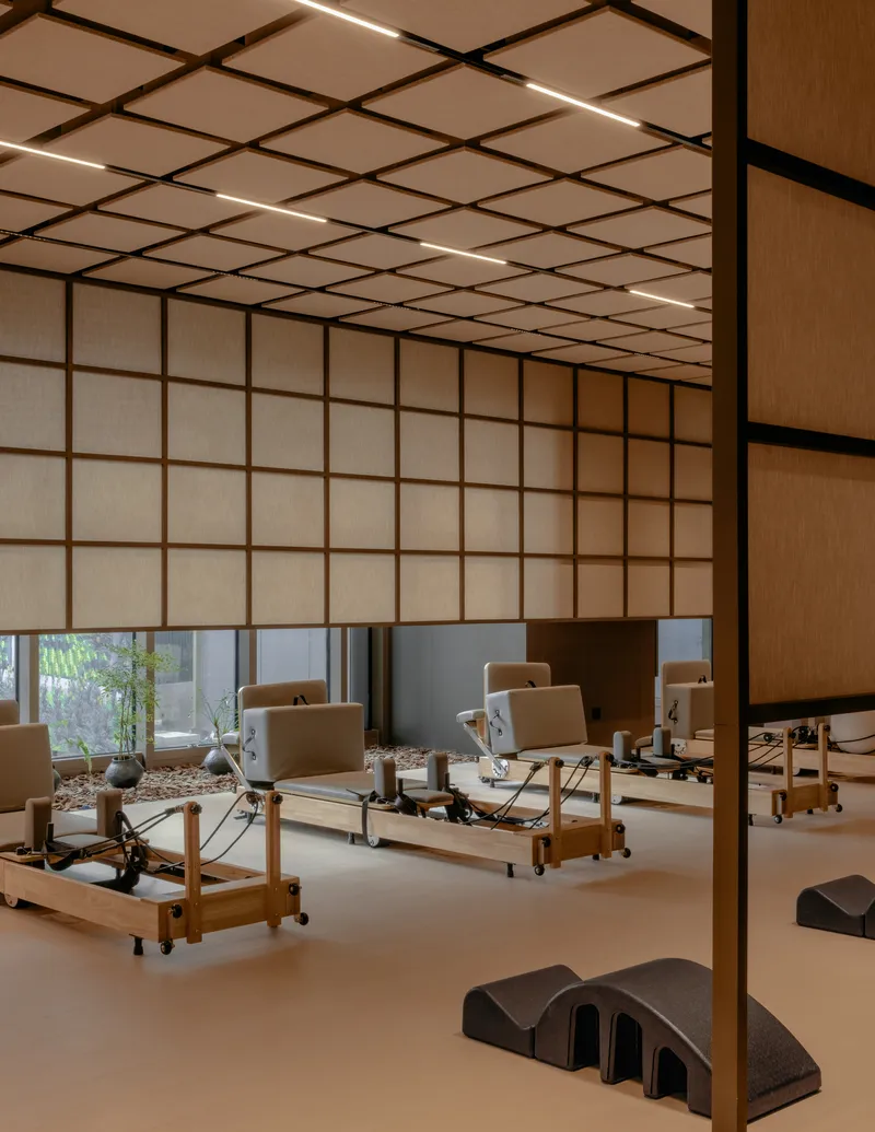 Pilates studio with wooden Reformer machines on pale floor beneath gridded translucent ceiling panels