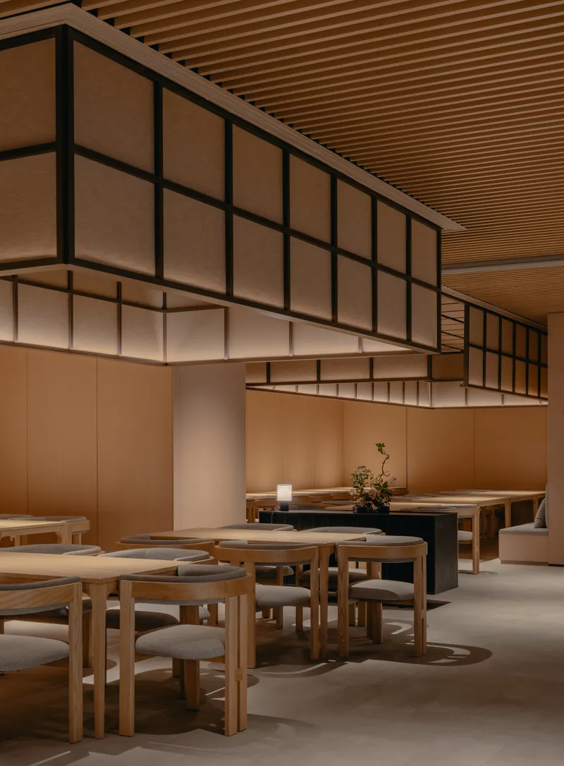 Dining hall with suspended translucent screens, slatted timber ceiling and grouped round tables on polished concrete