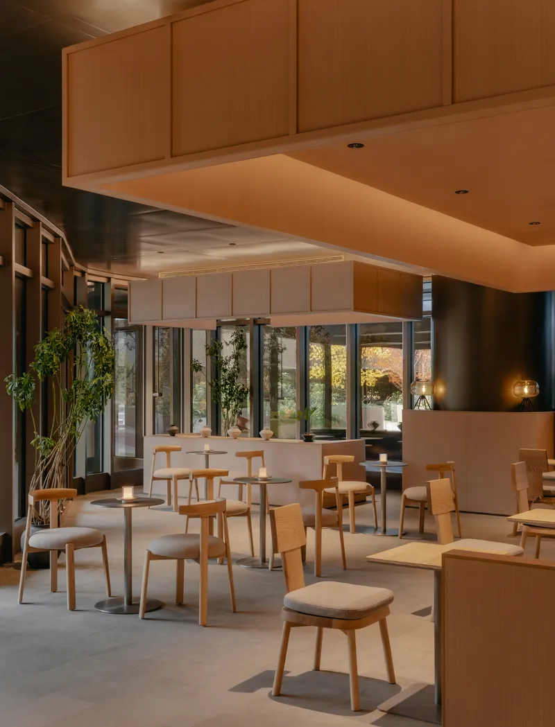 Dining zone under floating timber ceiling plane with glass wall revealing courtyard vegetation at twilight