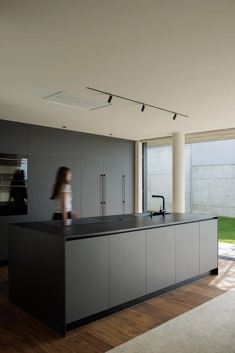 Kitchen island with black countertop as a figure passes through the sunlit space