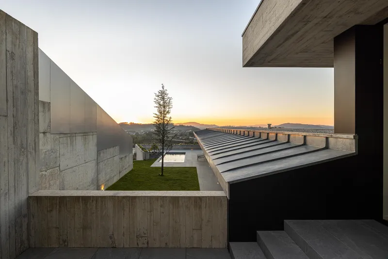 Upper-level courtyard framed by concrete volumes and steel staircase at twilight