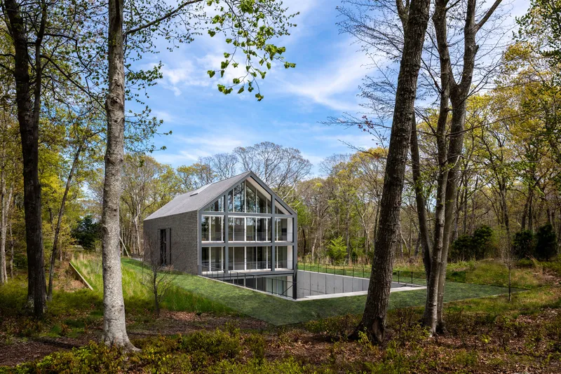Gabled volume with full-height glazing and slate terrace viewed through bare autumn trees