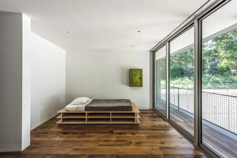 Bedroom with platform bed on wooden flooring and floor-to-ceiling glazing overlooking greenery