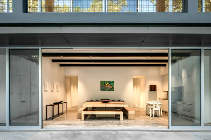 Open glass doors framing an interior gallery space with wooden benches and art on white walls