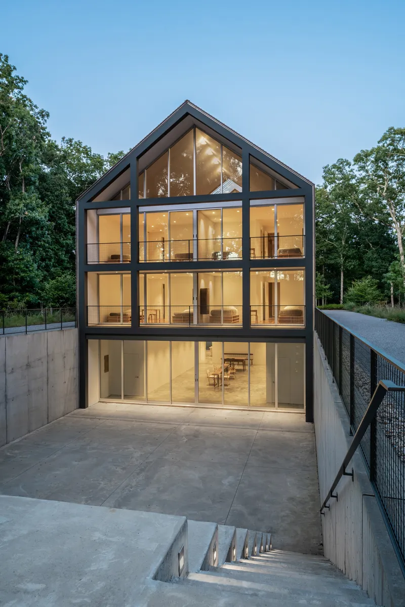 Rear gable facade with floor-to-ceiling glass panels and black steel framing at dusk