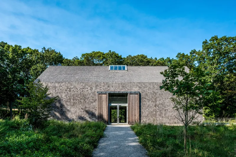 Cedar shingle facade with central glass entry door and roof monitor framed by dense oak trees