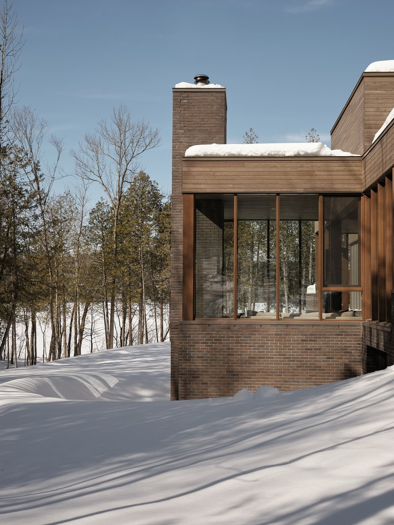 Brick and timber-clad volumes with a tall chimney rising above a snow-covered landscape in winter
