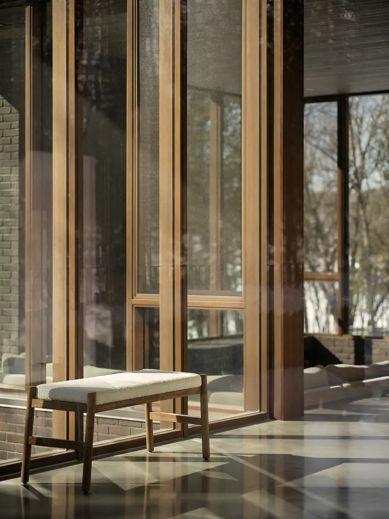 Timber-framed glass doors with a cushioned bench on polished concrete floors reflecting afternoon light