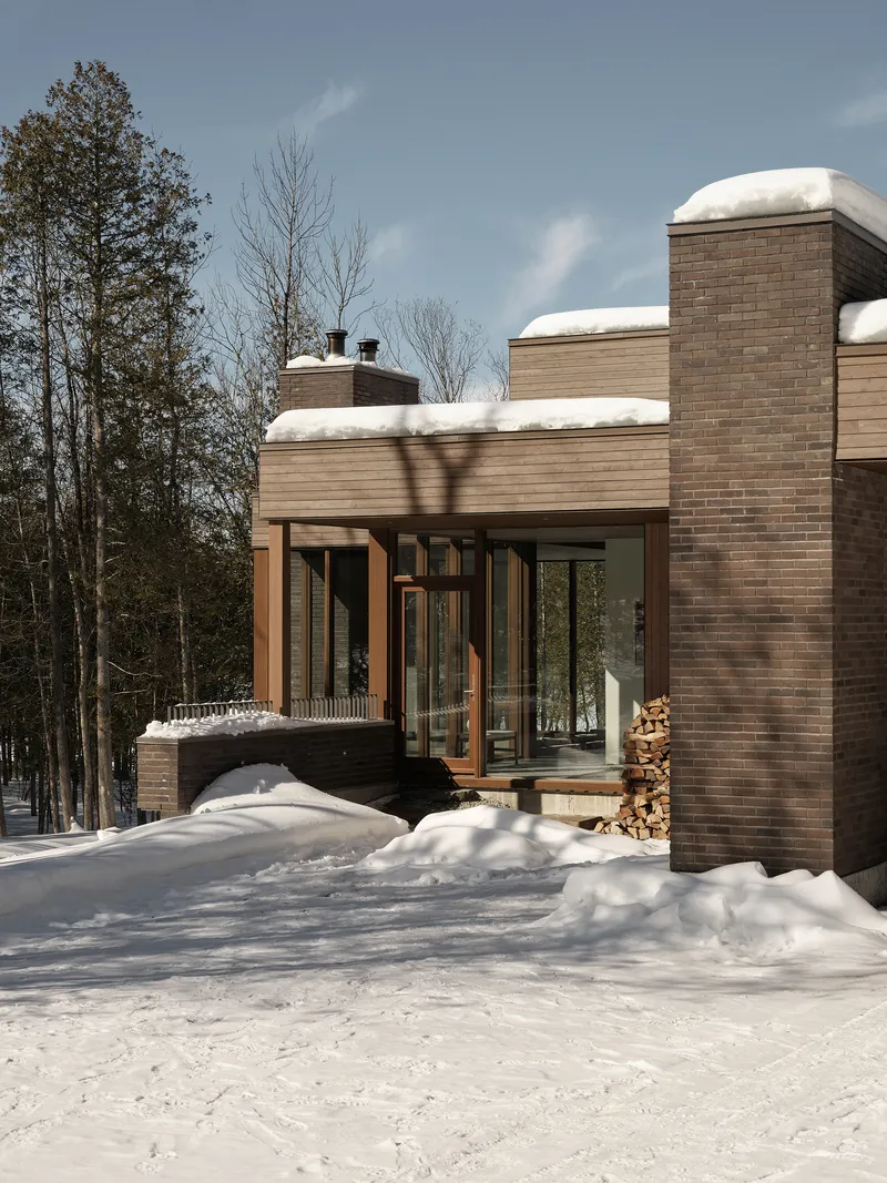 Entry terrace with timber-framed glass doors and stacked firewood beneath snow-capped rooflines