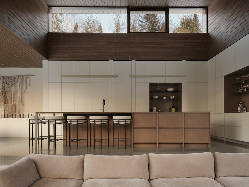Open-plan kitchen with bronze island and white cabinetry beneath horizontal clerestory windows