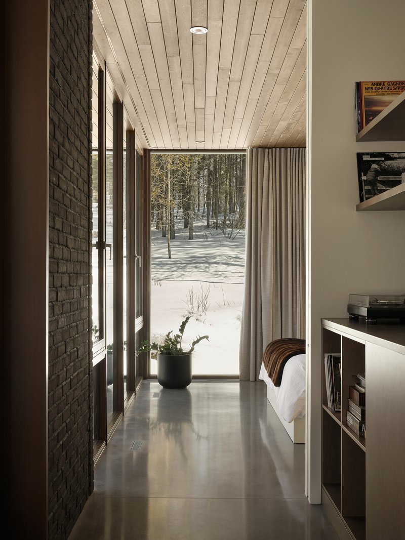 Hallway with dark brick wall and timber plank ceiling looking toward snow-covered birch forest