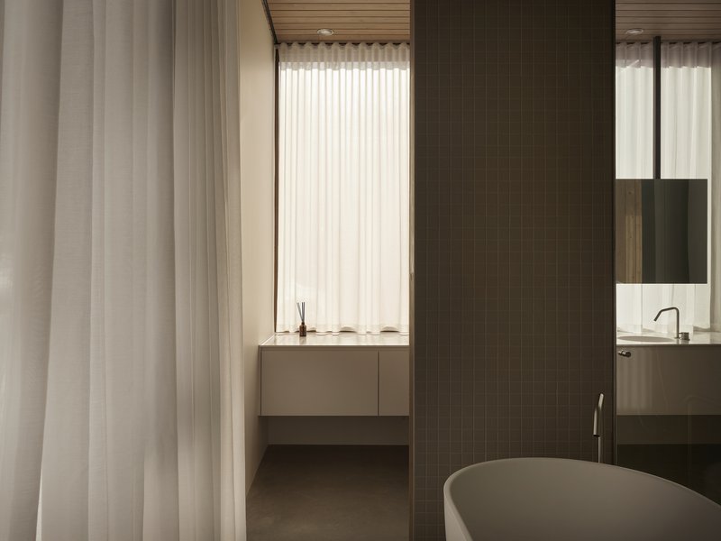 Bathroom view through curtain opening showing freestanding tub and timber tile partition wall