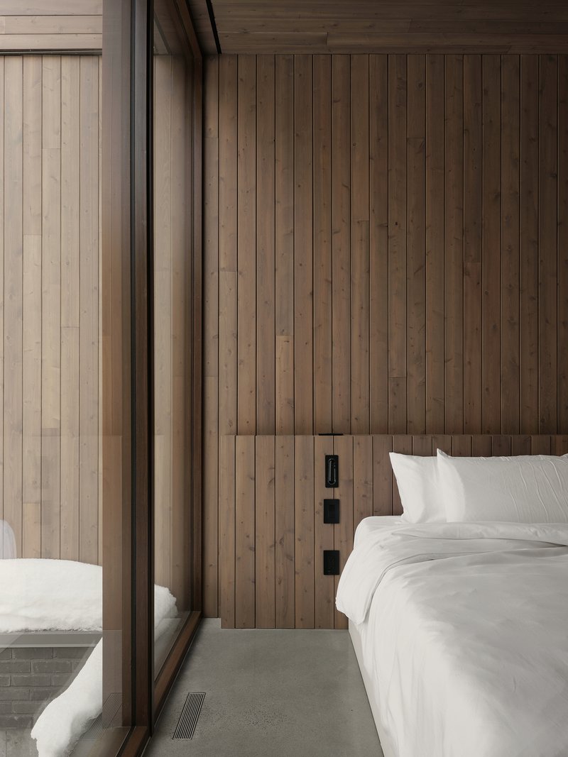 Bedroom interior with vertical timber plank wall and floor-to-ceiling glazing with white bedding
