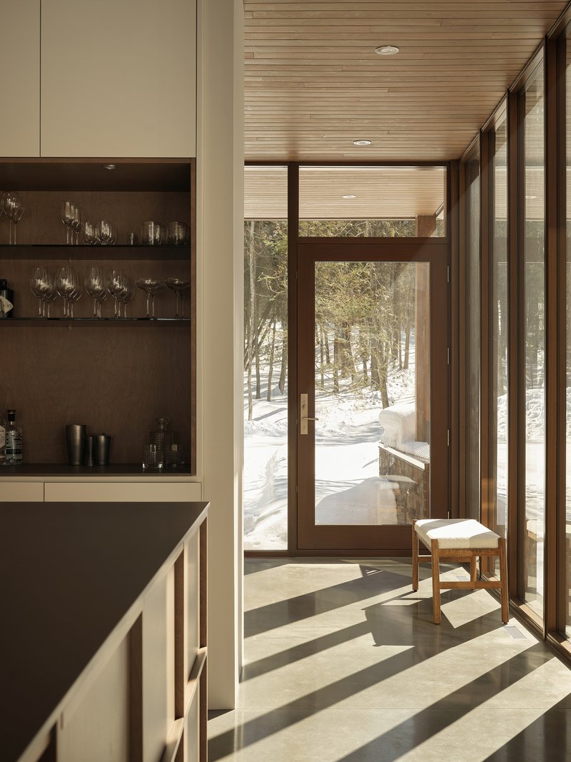 Entry hall with timber-framed glazing casting angular shadows on polished concrete floor in winter light