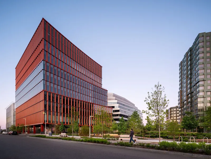Street view of the terracotta-clad facade with vertical fins beside landscaped median and pedestrian