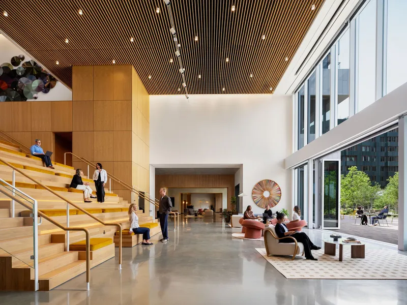 Double-height lobby with wood slat ceiling, tiered seating stair, and people gathering on polished concrete