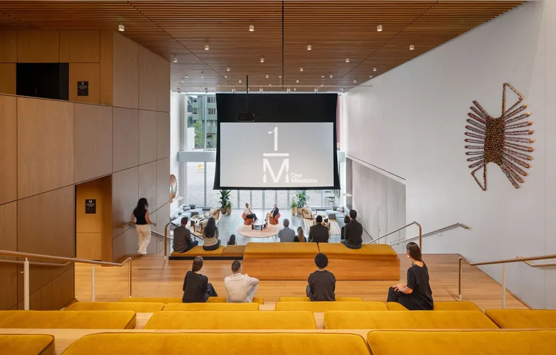 Tiered seating area with yellow cushions facing a projection screen and wall-mounted sculptural art piece