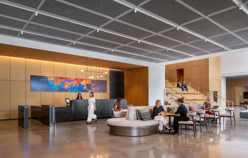 Lobby with perforated metal ceiling, curved reception desk, and timber-clad staircase with occupants in motion