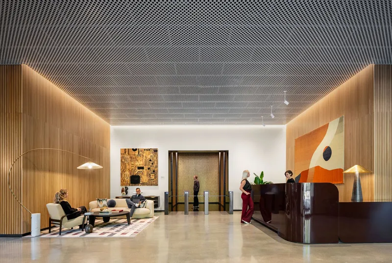 Reception hall with perforated metal ceiling, backlit wood walls, and curved dark wood desk