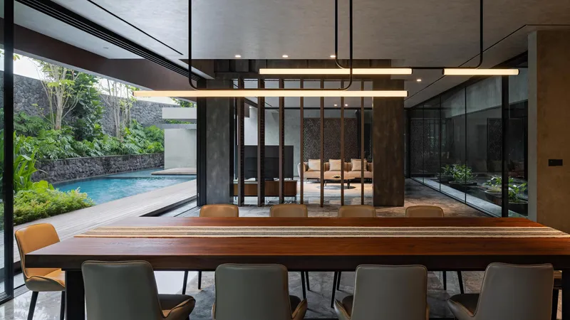 Dining room with timber table opening to pool terrace through floor-to-ceiling glazing and black steel frames