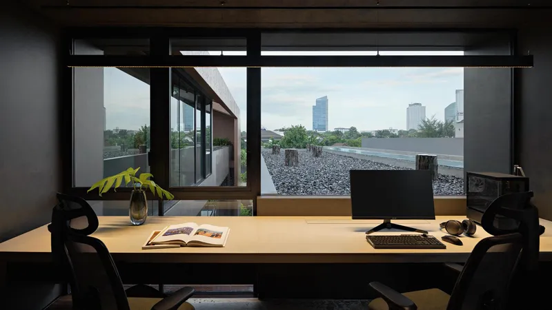 Home office desk facing a horizontal window with views of a gravel rooftop terrace and distant skyline