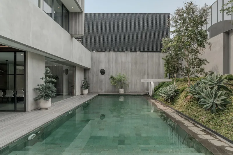 Courtyard pool surrounded by concrete walls, timber screens, and planted beds with agave and ornamental grasses
