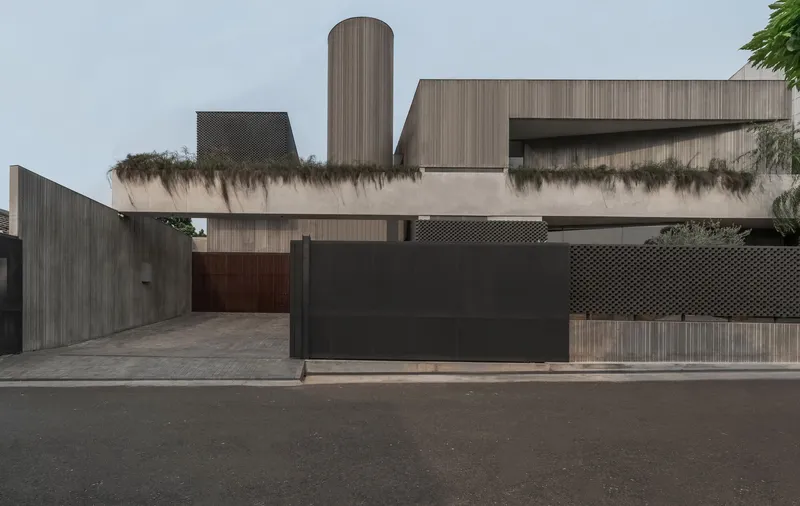 Street view of the residence with dark sliding gate, vertical timber cladding and cylindrical tower volume