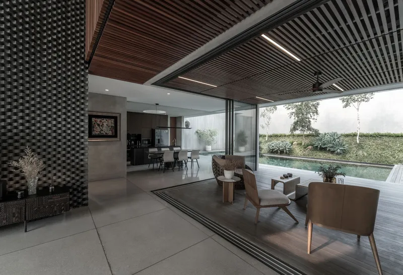 Open living space with slatted wood ceiling panels and floor-to-ceiling glass opening to the pool deck