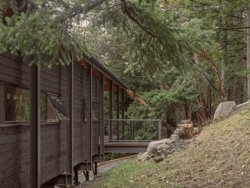 Dark-stained wood siding along exterior wall with sliding doors and metal railing beside sloped terrain