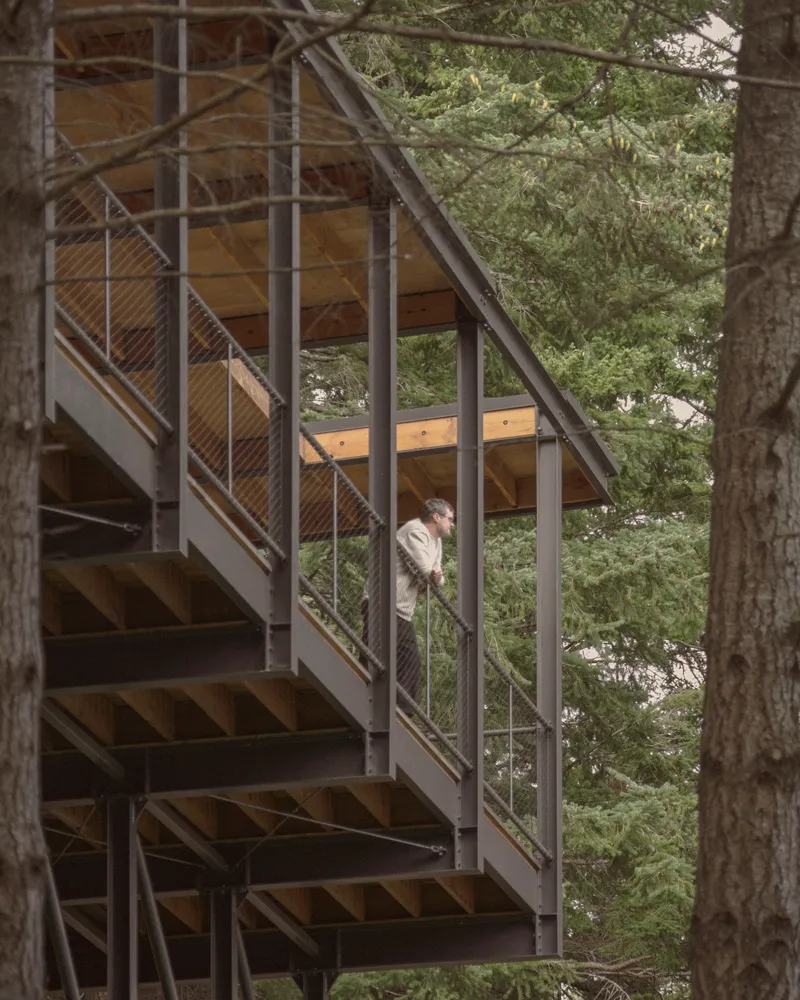 Zigzagging exterior stair with cable mesh railings and exposed timber beams beneath the roof overhang