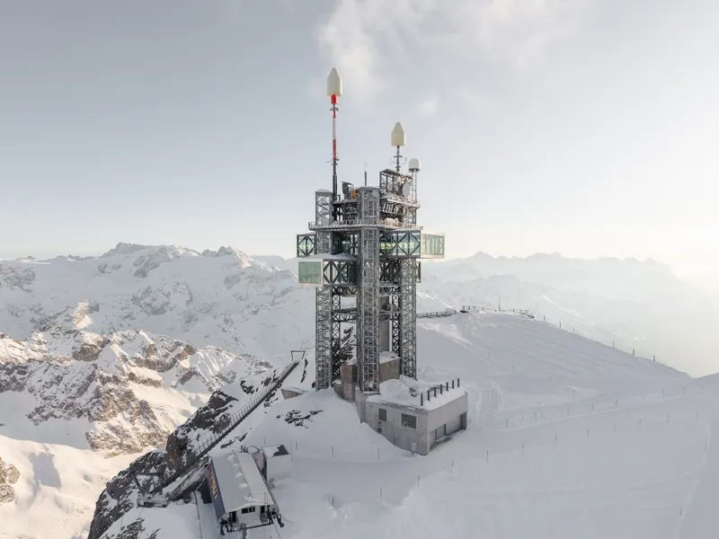 Aerial view of the galvanized steel transmission tower with antennas rising from a snowy mountain peak